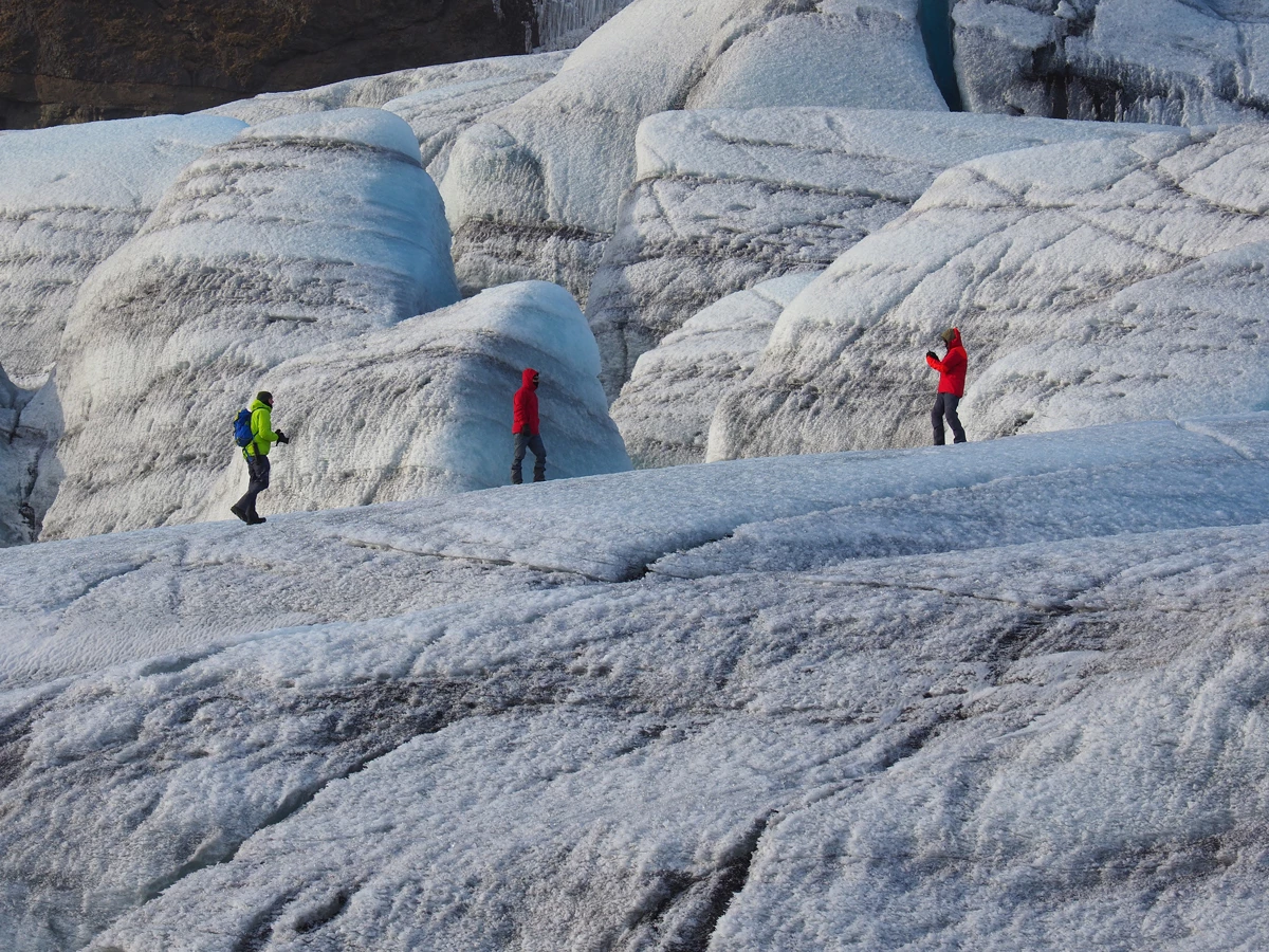 Three people in winter clothing hiking across a glacier